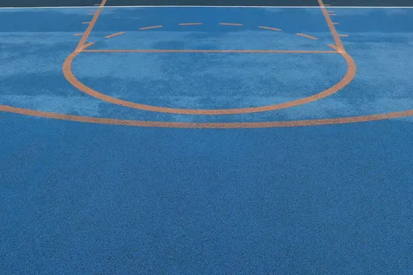 Basketbol işaretli ve ıslak yüzeyi turuncu yarı daireli renkli mavi spor sahasının en üst görüntüsü. Dokuya sahip kentsel atletizm alanı geçmişi