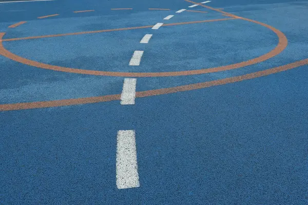 Kıvrımlı beyaz çizgi ve açık hava sahası yüzeyinde turuncu basketbol işaretleri, yağmurdan sonra ıslak desenli kauçuk döşemeli şehir oyun alanı manzarası.