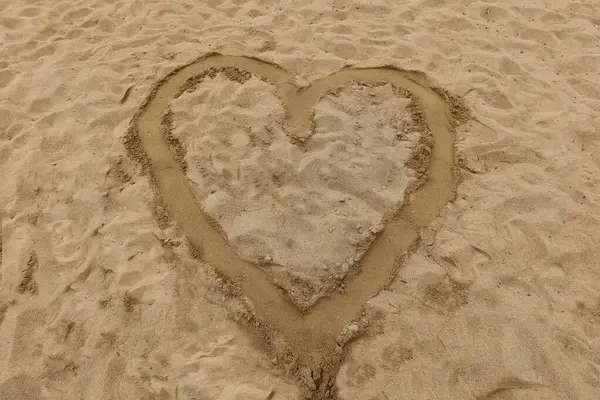 Plaj kumlarında kalp şekli, kumlu arka planda romantik bir sembol, aşk, tatil havası, özgürlük ve duygusal basitliği ifade ediyor.