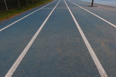 Beyaz şerit işaretli mavi koşu yolunun, sentetik yüzeyi ve spor dokusu olan açık hava atletizm alanının, doğal ışık altında boş çalışma alanının perspektifi