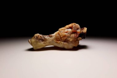 Asgari beyaz yüzeyde, dramatik ışıklandırmayla tek pişmiş tavuk budu. Yakından çekilen yemek görüntüsü kızarmış kümes hayvanlarının dokusunu, tadını ve basitliğini vurguluyor.