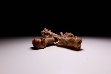 İki yenmiş tavuk budu kemiği, beyaz yüzeyde et kalıntıları ve koyu arkaplan. Minimalist gıda atığı konsepti, çarpıcı ışıklandırma ve gerçekçi mutfak detaylarıyla yakın plan..