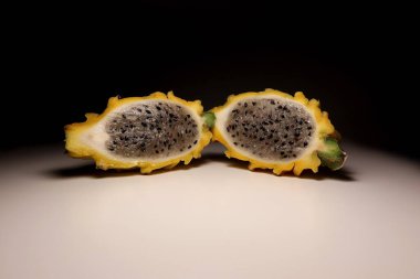 Taze sarı ejderha meyvesi (pitahaya), siyah tohumlu sulu beyaz posasını, nötr arkaplanda izole edilmiş olarak göstererek ikiye bölünmüştür. Sağlıklı gıda veya vegan konsepti için egzotik tropikal meyve makrosu