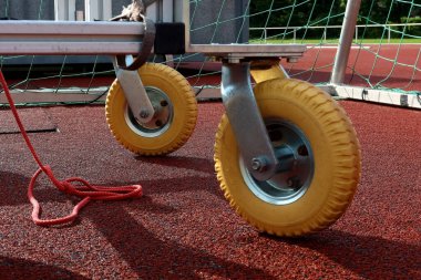 Kırmızı atletizm pistinde sarı lastik tekerleklerin yakın plan çekimi ve arka planda yeşil ağ var. Stadyum bakımı ya da spor tesisi desteği için araç gereç