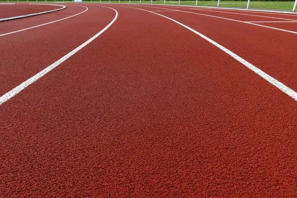Beyaz şerit işaretli kıvrımlı kırmızı koşu yolu. Temiz kauçuk yüzeyi olan boş bir açık hava atletizm pisti. Spor, zindelik, rekabet, motivasyon ve kararlılık kavramı