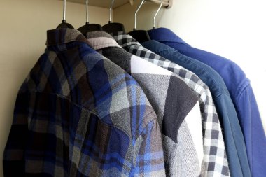 Ahşap gardıropta siyah askılar üzerinde günlük ekoseli ve katı gömlekler. Dolapta düzgün bir şekilde erkek kıyafetleri var. Günlük giyimde tekstil dokuları ve renk tonları