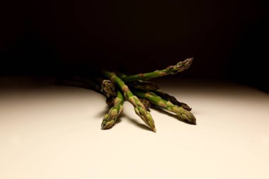 Taze yeşil kuşkonmaz mızrakları beyaz masada koyu arkaplanlı. Sağlıklı organik sebze, minimum gıda fotoğrafçılığı konsepti doğal ışıklandırma ve sığ alan derinliği.