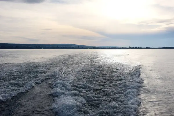 Şehir silueti ve yumuşak pastel gökyüzü ile sakin göl üzerinde gün batımı manzarası seyahat, doğa ve huzurlu ruh hali kavramları için mükemmel.