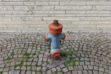 Eski kırmızı ve mavi yangın musluğu kaldırım taşı caddesinde bej tuğla duvarın önünde, tepeden tırnağa ön manzara, kentsel vintage detay