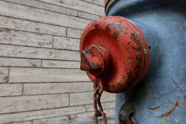 Eski mavi yangın musluğunun üzerindeki paslı kırmızı valf ve metal zincir ile dokulu taş duvar zemininin yakın görüntüsü. Kentsel ayrıntı ve klasik sanayi altyapısı