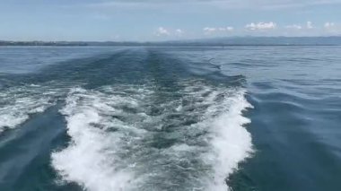 Köpüklü tekne huzurlu mavi gölde güneşli gökyüzünün altında uzak ormanlık kıyı ve dağlarla kalkıyor. Yolculuk, macera, tekne, yaz tatili, doğa ve su sporları temaları için mükemmel.