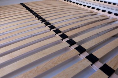 Modern bir yatak çerçevesinde siyah plastik tutacakları olan ahşap yatak çatalları, döşek için yapı ve destek sistemini gösteriyor. Açık detaylarla yatay perspektif