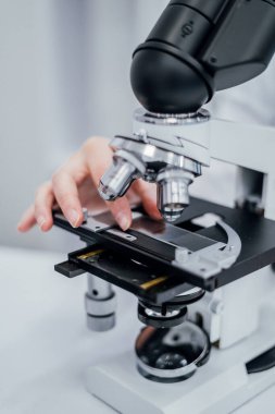 Bir araştırmacı tarafından dikkatlice ayarlanan mikroskop kaydırak sahnesinin yakından görüntüsü. Görüntü, laboratuvar ortamlarında gerekli detaylara hassasiyet ve dikkati vurgular,