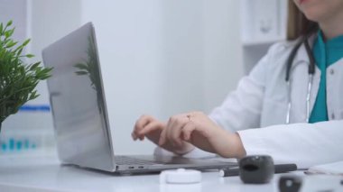 Parlak ve düzenli bir ofiste dizüstü bilgisayarla çalışan bir doktor. Boynunda steteskop olan beyaz bir önlük giyerek, profesyonelliği ve kendini adamışlığı yansıtan perdeye dikkatle odaklanıyor.