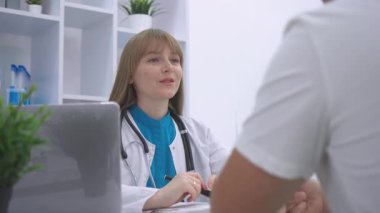 Profesyonel bir kadın doktor muayene sırasında hasta kayıtlarını dikkatle inceler. Bir dizüstü bilgisayar, laboratuvar aletleri ve organize raflar ile donatılmış sağlık ofisi, modern ve