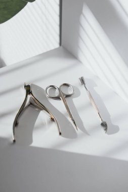 Düz metal manikür aletleri. Tırnak ucu, makas ve itici. Güneş ışığı altında yerleştirilmiş. Güzellik ve kişisel bakım temaları için ideal minimalist kompozisyon.