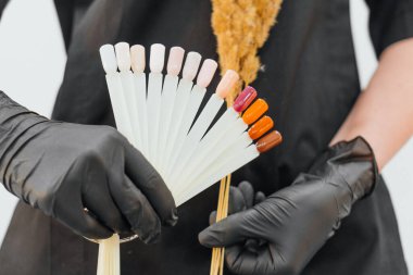 Siyah eldivenlerle sergilenen canlı tırnak cilası koleksiyonu. Gölgeler yumuşak pastellerden koyu portakal ve kahverengilere kadar değişiyor, şık ve profesyonel bir sunum oluşturuyor.
