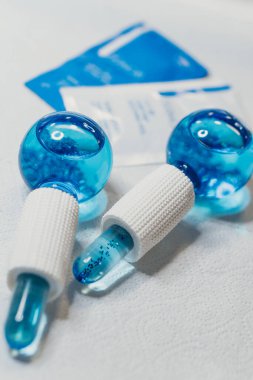 Beyaz saplı ve deri kesesi olan iki mavi cam masaj küresi yeni bir spa atmosferi yaratır. Beyaz arka planda deri kesesi olan mavi cam masaj küreleri.