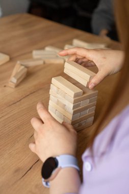 Eller ahşap bir kule inşa ediyor, takım çalışmasını, stratejiyi ve eğlenceyi sembolize ediyor. Aile oyunu geceleri ya da dostça mücadeleler için mükemmel