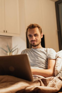 Bir adam evinde huzurlu bir akşamın keyfini çıkarır, bilgisayarını internet bağlantısı olarak kullanır. Ilık aydınlatma rahatlama, sevgi ve dijital bağlılık atmosferini vurgular