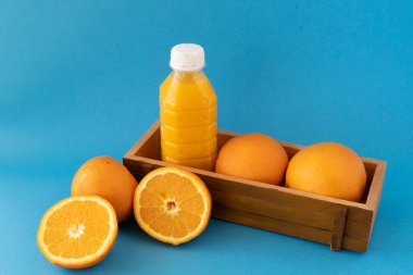 Portakal tutan ahşap bir kutu ve meyve suyu şişesi olan canlı bir düz yatak sahnesi dilimlenmiş narenciye ile mavi bir zemin üzerine kurulmuş. Beslenme blogları, meyve suyu barları ya da sağlıklı yaşam tarzı için mükemmel.