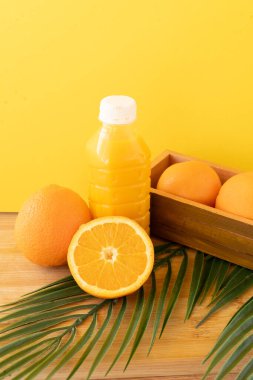Taze narenciye meyveli portakal suyu şişesi ve ahşap tahtada parlak sarı arka planlı palmiye yaprağı. Yüksek kalite fotoğraf