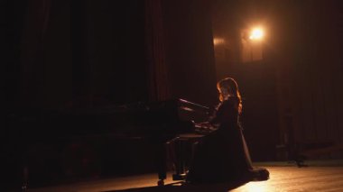 Bir Grand Concert Hall 'da dramatik Solo Piyano Performansı A piyanisti loş bir konser salonunda tek başına piyano çalar. Tek bir spot ışığı onun siluetini vurguluyor, duygusal ve...