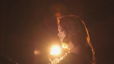 Dramatik arka ışıklandırmayla aydınlatılmış, sinematik bir siluet yaratan bir piyanist. Altın parıltı performansın zarafetini ve duygusunu artırırken, ışık yansımaları rüya gibi, sanatsal bir şey ekliyor.