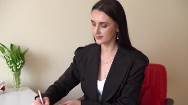 Siyah takım elbiseli bir kadın deftere notlar yazar. İş stratejisi, şirket planlaması ve anahtar kavrayışlar hazırlar. Organizasyon ve verimliliğe odaklanmış modern bir profesyonel ortam.