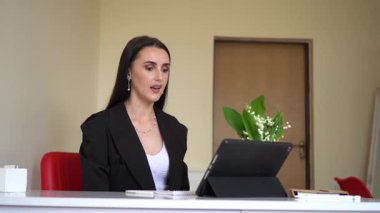 İş elbisesi giymiş profesyonel bir kadın tabletle online toplantı yapıyor strateji, paydaşlar ve tedarik konularını tartışıyor. Yeni bir çiçek dokunuşuyla modern ofis dekoru zarafet katar..
