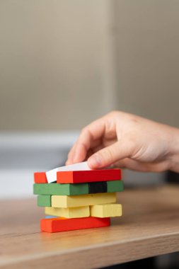 Renkli parçalar yığınına bir blok koyan bir el büyümeyi, yaratıcılığı ve problem çözmeyi sembolize ediyor. Eğitim faaliyetlerini ya da interaktif öğrenimi desteklemek için mükemmel