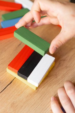 Bir el, yeşil bloğu, interaktif oyun yoluyla odak, öğrenme ve beceri geliştirmeyi temsil eden renkli bir yığın üzerine dikkatlice yerleştirir. Eğitim araçları ve yaratıcı faaliyetler için ideal