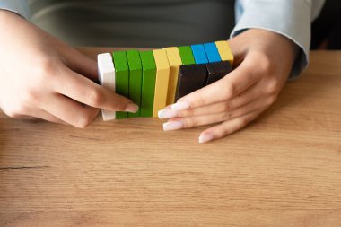 Eller ahşap bir masanın üzerine renkli yeşil, sarı ve siyah bloklar dizer. Stratejik düşünmeyi ve pratik öğrenmeyi sembolize eder. Takım çalışması, yaratıcılık ve eğitim materyalleri için mükemmel bir örnekleme