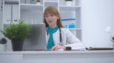 Steteskoplu tıp üniformalı bir kadın bilgisayarını kullanarak uzaktan kumandalı modern teletıp teknolojisi ile hastalarla çevrimiçi iletişim kuruyor.