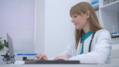 Kendine güvenen kadın doktor, modern teknoloji ortamında dijital sağlık süreçlerine, teletıp haberleşmelerine ve hasta veri yönetimine odaklanmış, parlak klinik iç mekanlarında dizüstü bilgisayar kullanıyor.