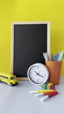 Tebeşir tahtası ve kırtasiyeli neşeli çalışma alanı. İçinde bir karatahta, renkli kırtasiye malzemesi, bir saat ve oyuncak okul otobüsü olan canlı bir çalışma alanı. Arka plan parlak sarı, neşeli bir...