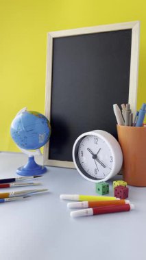 Parlak sarı arka planda bir küre, bir saat ve kırtasiye malzemesinin yer aldığı renkli bir çalışma alanı. Sahne bir karatahta, kalem ve zar içeriyor, eğitici bir atmosfer yaratıyor. Renkli Educa