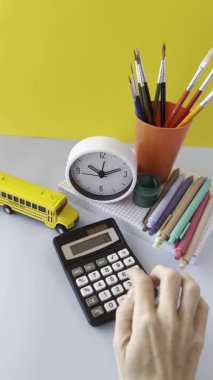 Çalışma alanı sahnesinde hesap makinesi, saat, renkli kalemler ve oyuncak okul otobüsü var. Arka plan parlak sarı, neşeli bir atmosfer yaratıyor. Hesap makinesi ve Statione ile Renkli Çalışma Alanı