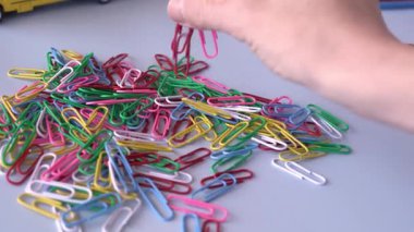 Arka planda mor bir zımba ve kalemle bir masaya saçılmış renkli ataçlara uzanan bir el. Olay yeri bir organizasyon ve ofis malzemesi hissi veriyor. Renkli Kağıt Tıkacı Kapalı