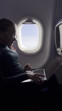 Dişi gezgin, uçuş sırasında sakin çalışma saatlerinden hoşlanır. Laptop açık kahve, pencerenin önünde durur. Hareket kabiliyeti ve farkındalığın hafif dengesi.