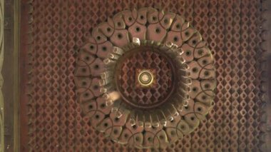 Ayrıntılı oymalar ve merkezi aydınlatma armaşıyla dairesel desenli karmaşık bir tavan tasarımı. Sıcak tonlar ve geometrik şekiller büyüleyici bir görsel etki yaratır..