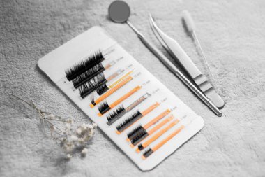 Birkaç kirpik uzatma bandı temiz beyaz bir yüzey üzerinde eşsiz kıvrımlar ve uzunluklar göstererek güzellik tedavilerinde göz estetiğini geliştirmek için seçenekleri vurguluyor. Kirpik uzantılarının kapatılması