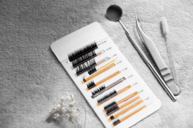 Cımbız, fırça ve ayna gibi güzellik aletlerinin yanı sıra, bir kartta gösterilen kirpik uzantılarının yakın çekim görüntüsü. Arka plan yumuşak ve dokulu. Güzellik temasını geliştiriyor..