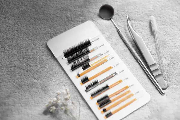 Cımbız, fırça ve ayna gibi güzellik aletlerinin yanı sıra, bir kartta gösterilen kirpik uzantılarının yakın çekim görüntüsü. Arka plan yumuşak ve dokulu. Güzellik temasını geliştiriyor..