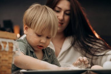 Genç bir çocuk, annesiyle birlikte un çiziyor, duygusal gelişimi, yaratıcılığı ve evde günlük ebeveynliğin neşeli ritüellerini destekleyen dağınık bir oyun anını paylaşıyor.