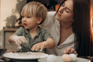Bir anne ve çocuğu arasında sakin bir an. Bebek unla oynarken. Mutfak sahnesinde karışıklık ve neşe yaratırken.
