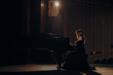 Zarif bir piyanist loş bir tiyatro sahnesinde büyük bir piyanonun başında oturur. Yumuşak spot ışıkları onun zarif formunu aydınlatıyor, sakin ve sanatsal bir atmosfer yaratıyor..