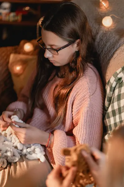 Uzun saçlı ve gözlüklü genç bir kız rahat bir kış akşamında rahat bir köşede yumuşacık ipliklerle el işi yapıyor. Peri ışıklarıyla aydınlatılıyor. Huzurlu bir kış anı, son derece odaklanmış genç bir kızı gösteriyor.