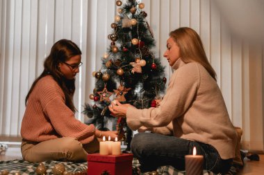 Anne ve kızı süslenmiş bir Noel ağacının yanına oturmuş mum ışığı yanlarındaki yavaş yaşayan aile bağlarını ve nostaljik festival geleneklerini simgelerken el yapımı süsler asıyor.
