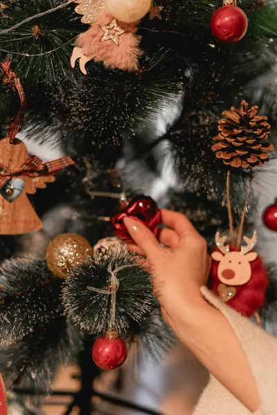 Noel ağacını süslerle süslemek bir yılbaşı ağacını kırmızı ve altın takılar, ahşap süslemeler ve çam kozalaklarıyla süslemek. Sahne bir şeyi çağrıştırıyor.